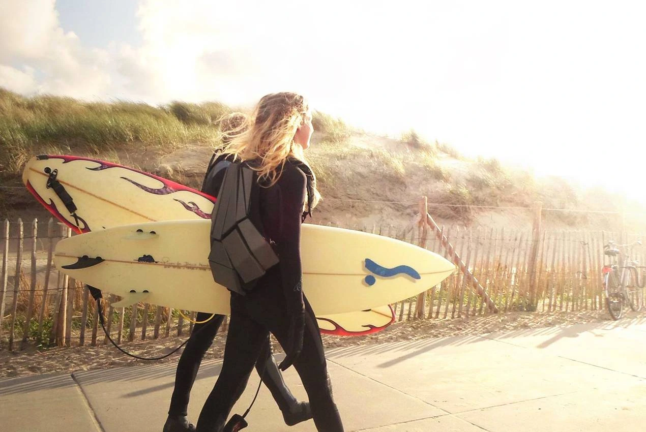 REK backpack worn while carrying a surfboard near the coast